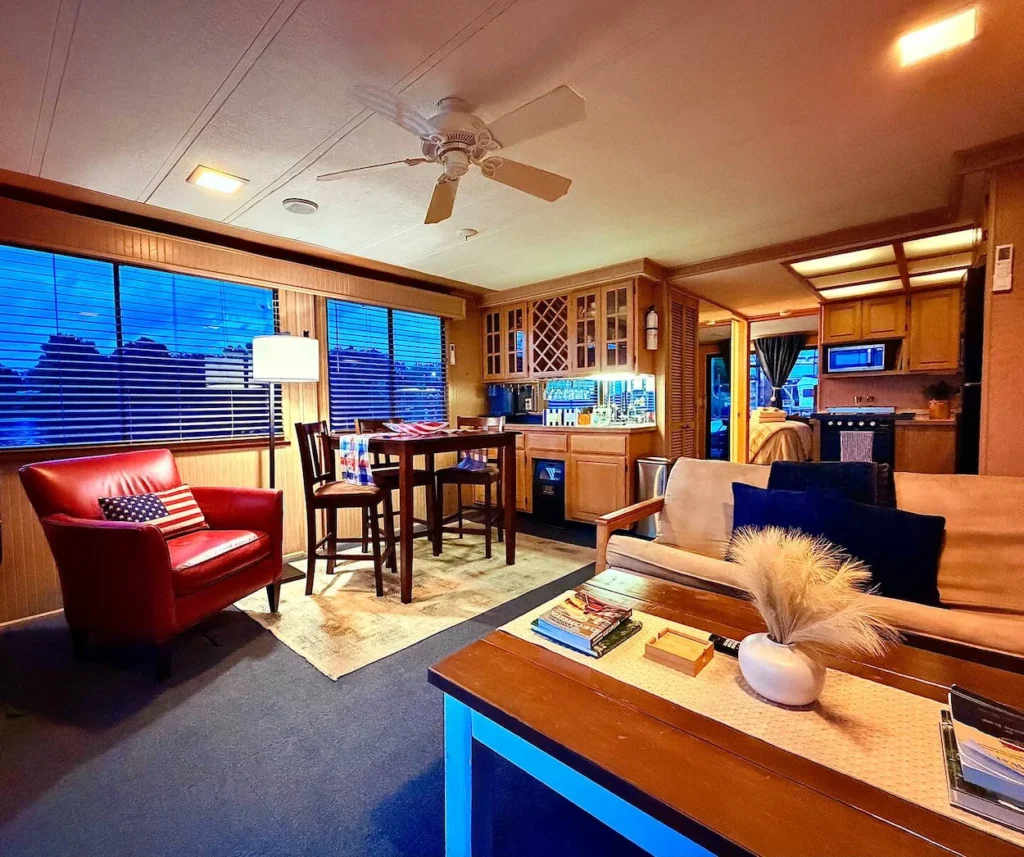 Cozy houseboat interior with a red armchair, dining high-top, kitchen, and living room seating