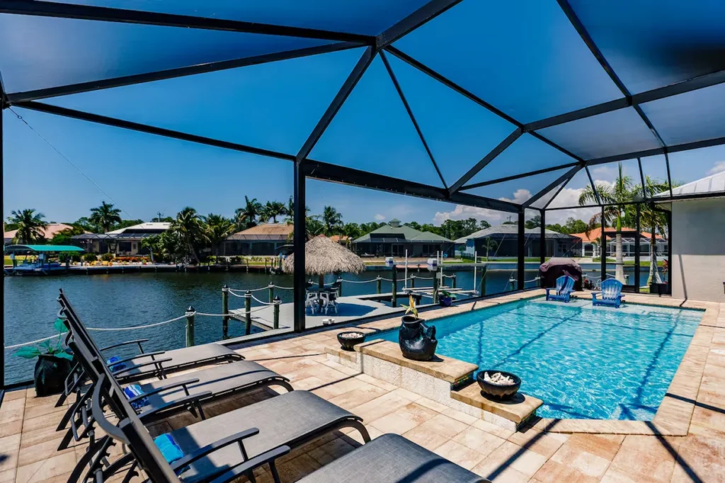 Screened-in lanai with a swimming pool and lounge chairs overlooking a canal and private boat dock