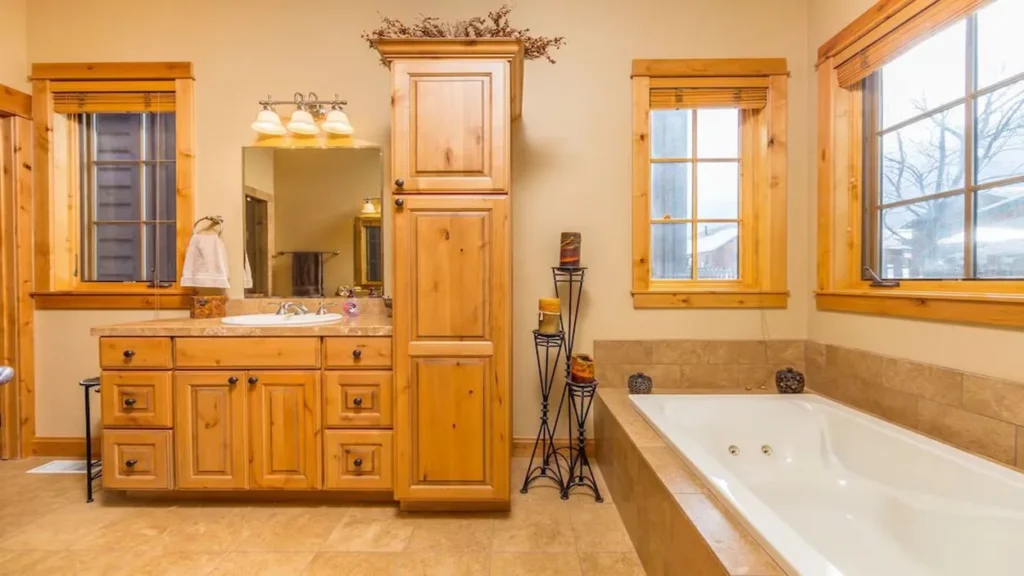 A rustic cabin bathroom featuring a large white bathtub next to light-colored wooden cabinets and a vanity