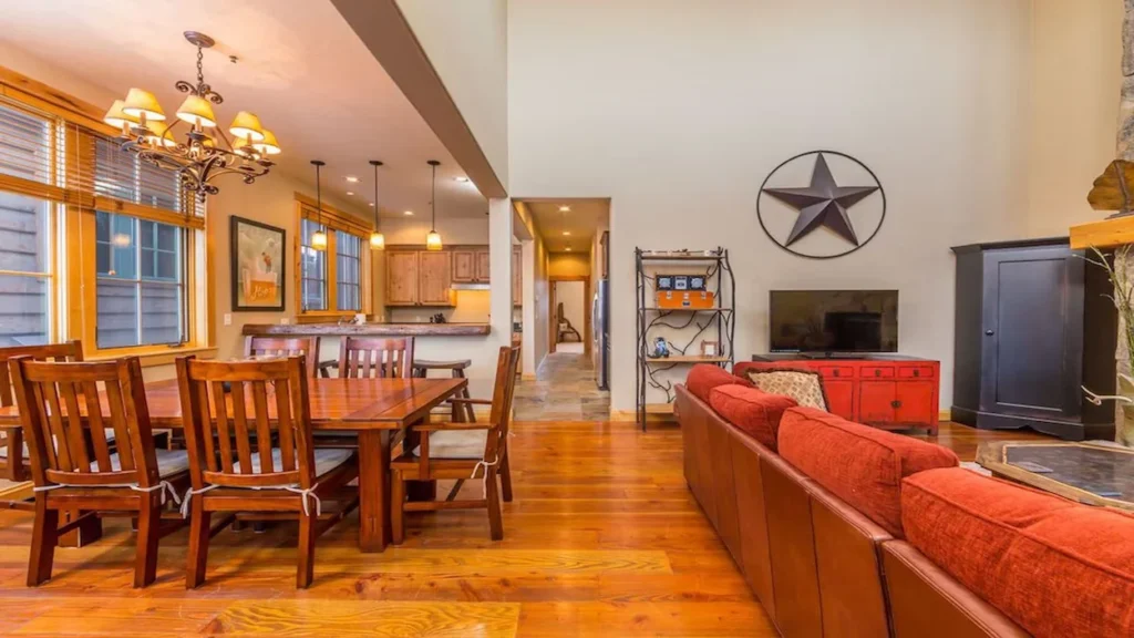 An open cabin interior with a wooden dining table, red sectional sofa, and a wall-mounted star decoration