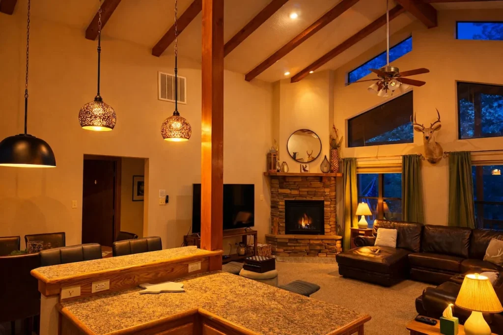 A cozy cabin living room with a stone fireplace, leather sectional sofa, and hanging pendant lights