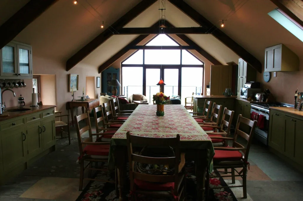 Spacious lodge kitchen and dining area under a vaulted ceiling with a long dinner table leading toward floor-to-ceiling windows