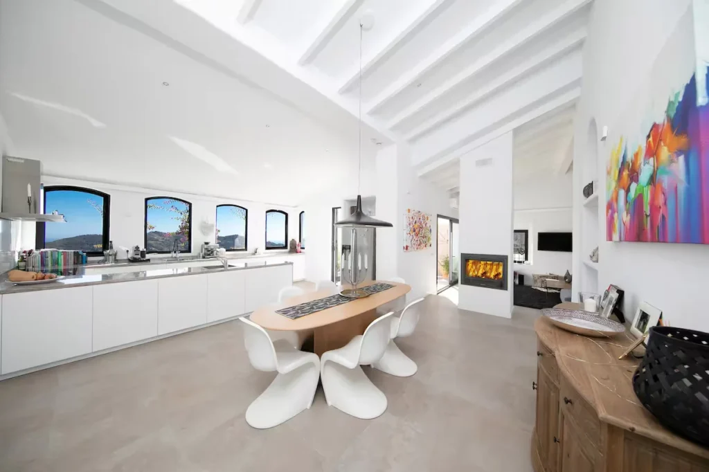 Bright modern villa kitchen with a wooden dining table, white chairs, and arched windows