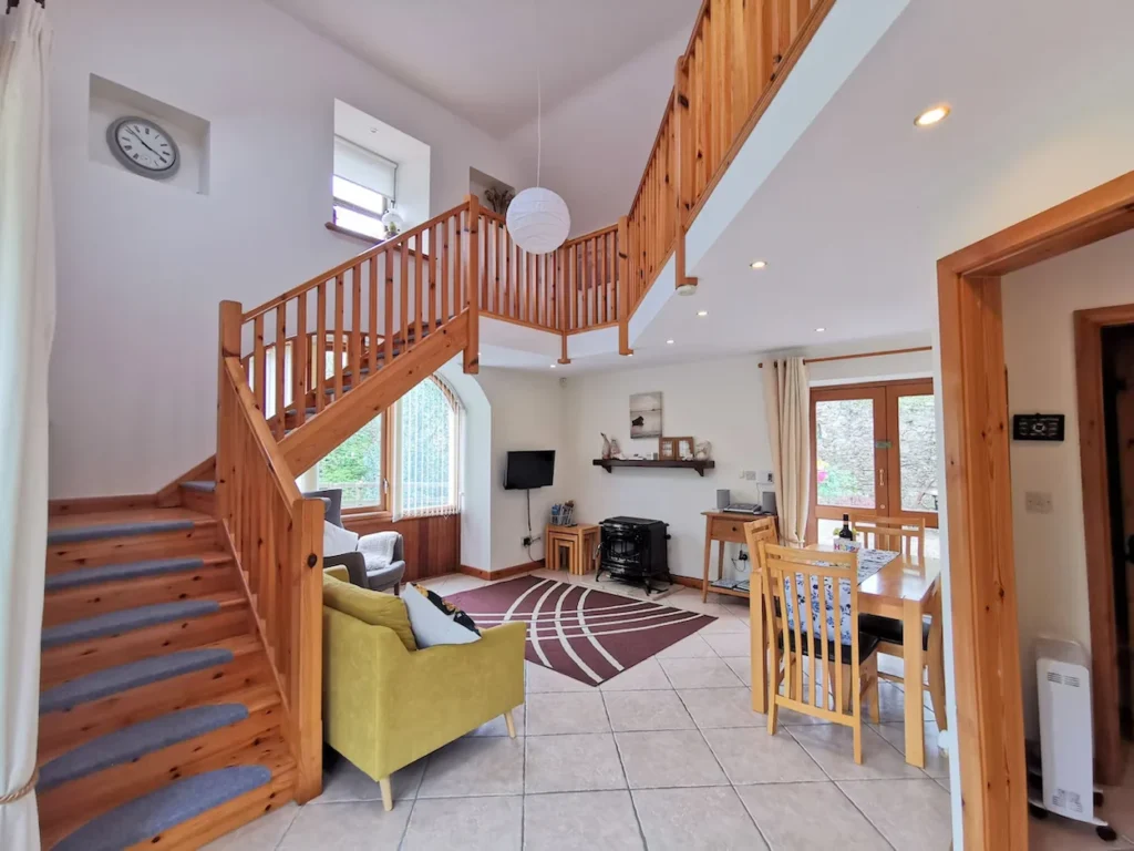 Open-plan cottage living room with a prominent wooden staircase leading to an upper mezzanine level