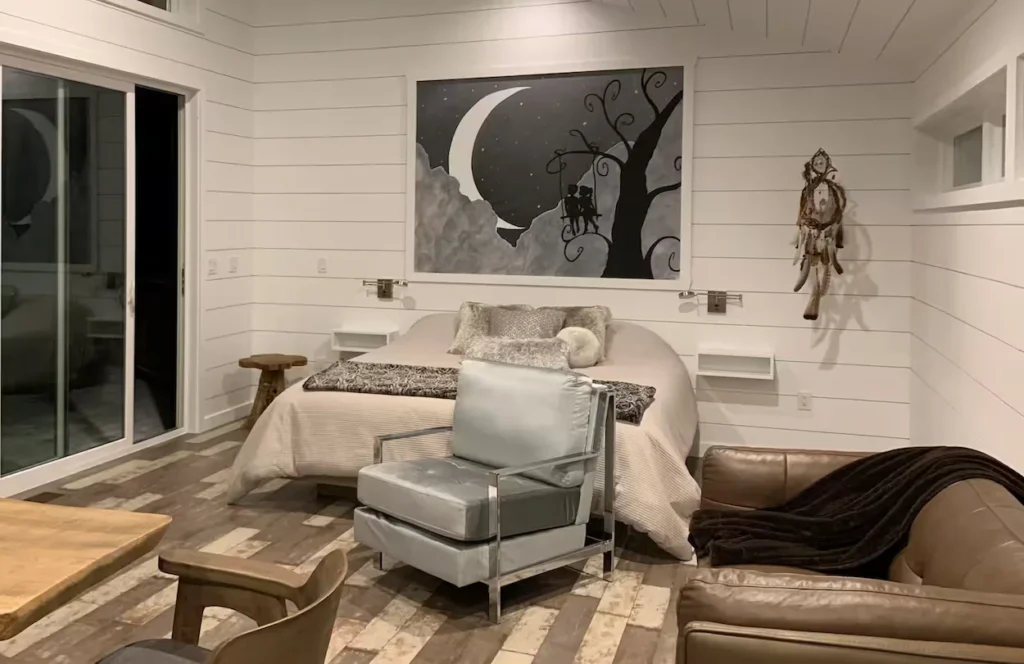 Bedroom with shiplap walls, a large moon painting over the bed, and a grey armchair