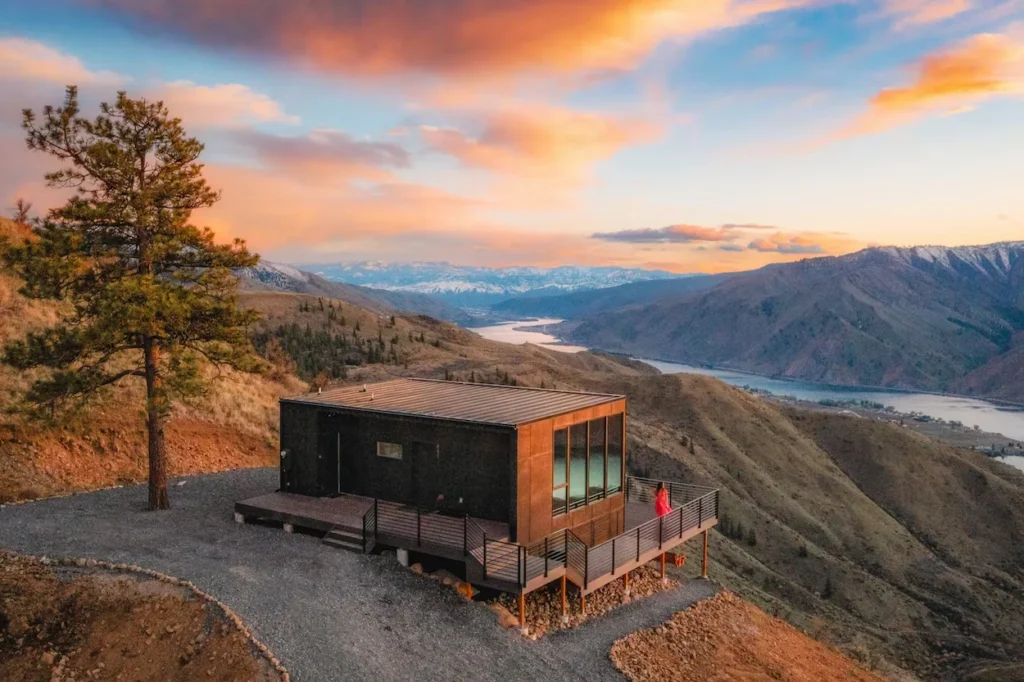 Modern dark wood cabin on a mountain ridge overlooking a river valley