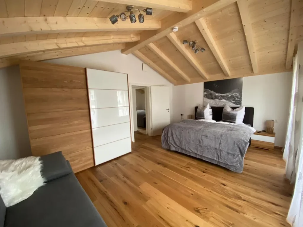 Modern alpine bedroom with vaulted wood ceilings, a large bed, and a wooden sliding wardrobe