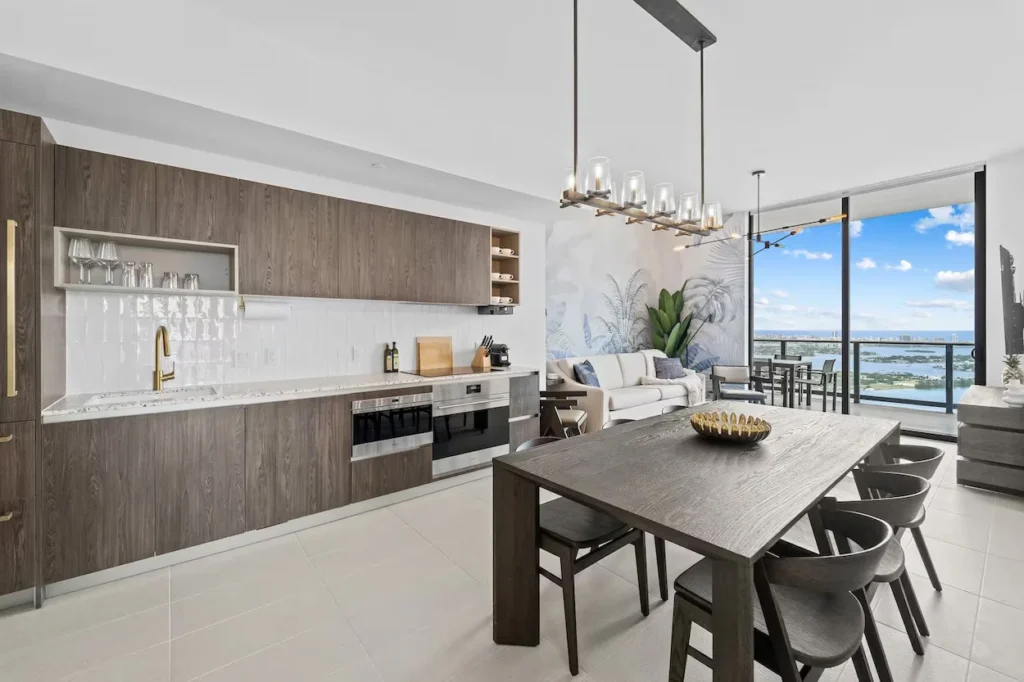 Modern open-concept kitchen and dining area with wood cabinets and a balcony overlooking water