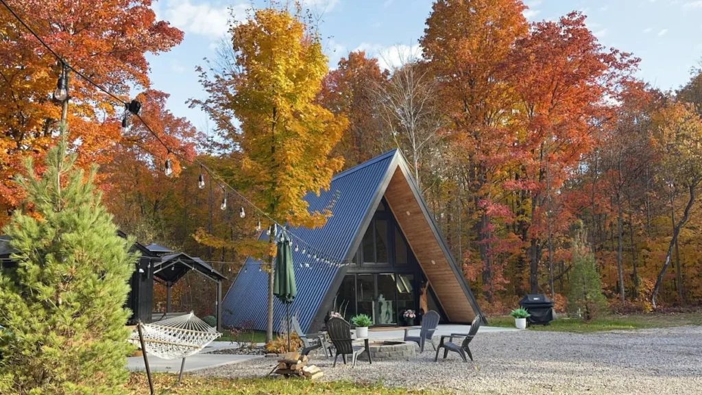Black metal A-frame cabin with a patio fire pit surrounded by autumn trees