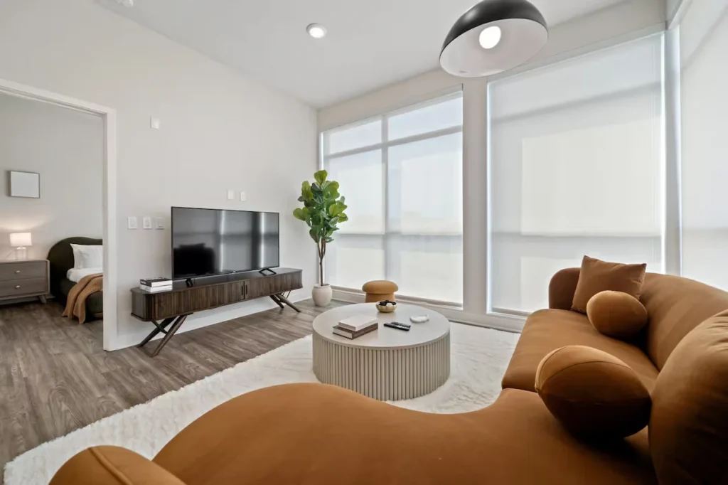 Modern penthouse living room with a curved brown sofa, flat-screen TV, and large windows