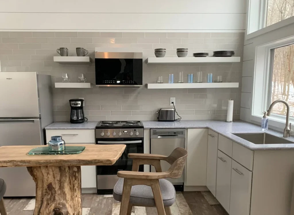 Modern kitchen with grey subway tile, open floating shelves, and a live-edge wood table