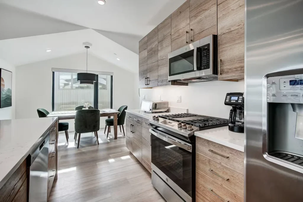 Modern kitchen with light wood cabinets, stainless steel appliances, and a dining table