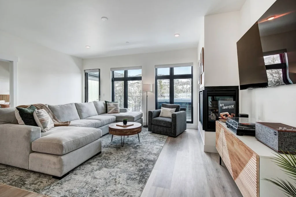 Modern white penthouse living room with a large gray sectional, fireplace, and flat-screen TV
