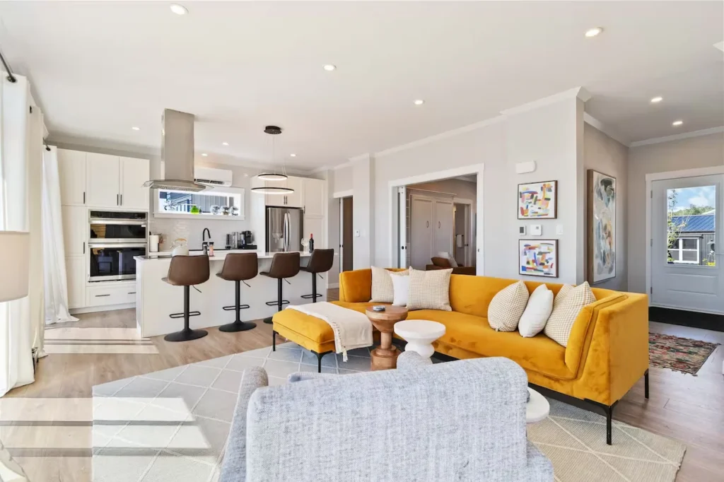 Modern open layout interior with a yellow velvet sectional sofa, gray armchair, and white kitchen