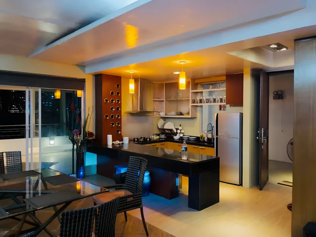 Modern penthouse kitchen with a black breakfast bar counter, glass dining table, and stainless refrigerator