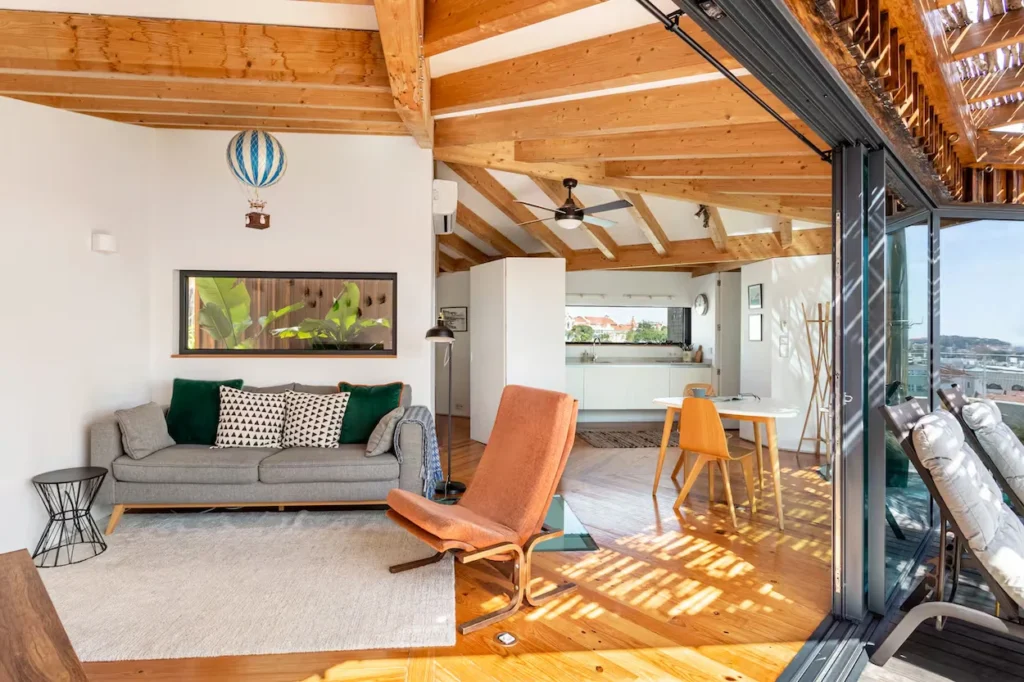 Bright modern living room with a grey sofa, orange armchair, and exposed timber ceilings