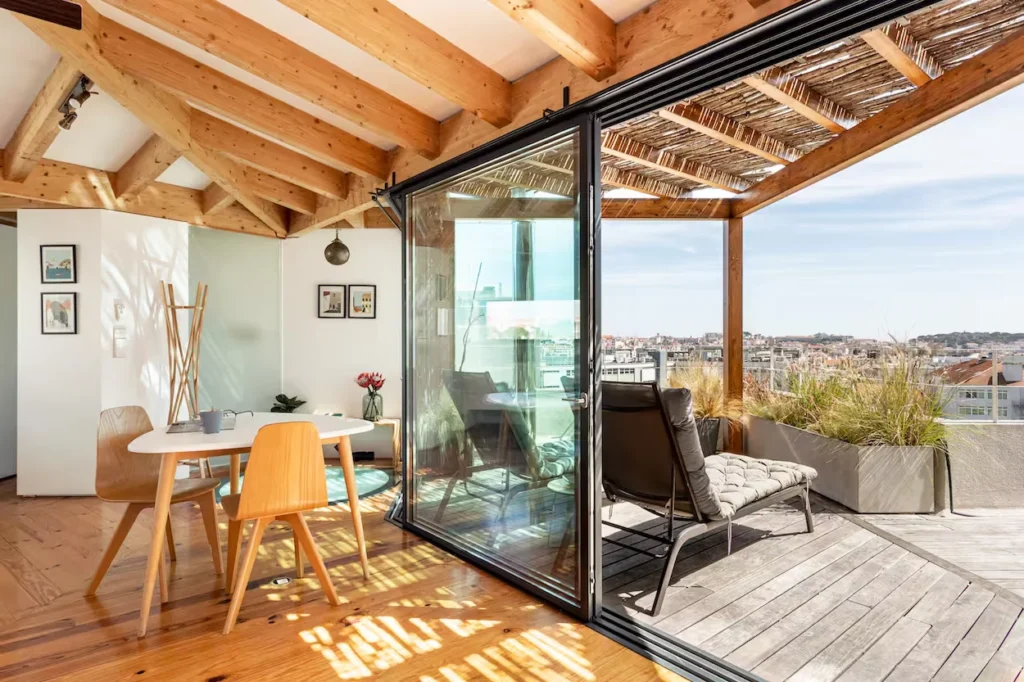 Bright penthouse interior opening onto a wooden rooftop deck with lounge chairs and city views