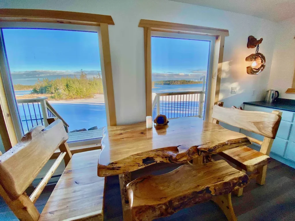 Live edge wooden dining table and benches next to large windows overlooking a frozen river