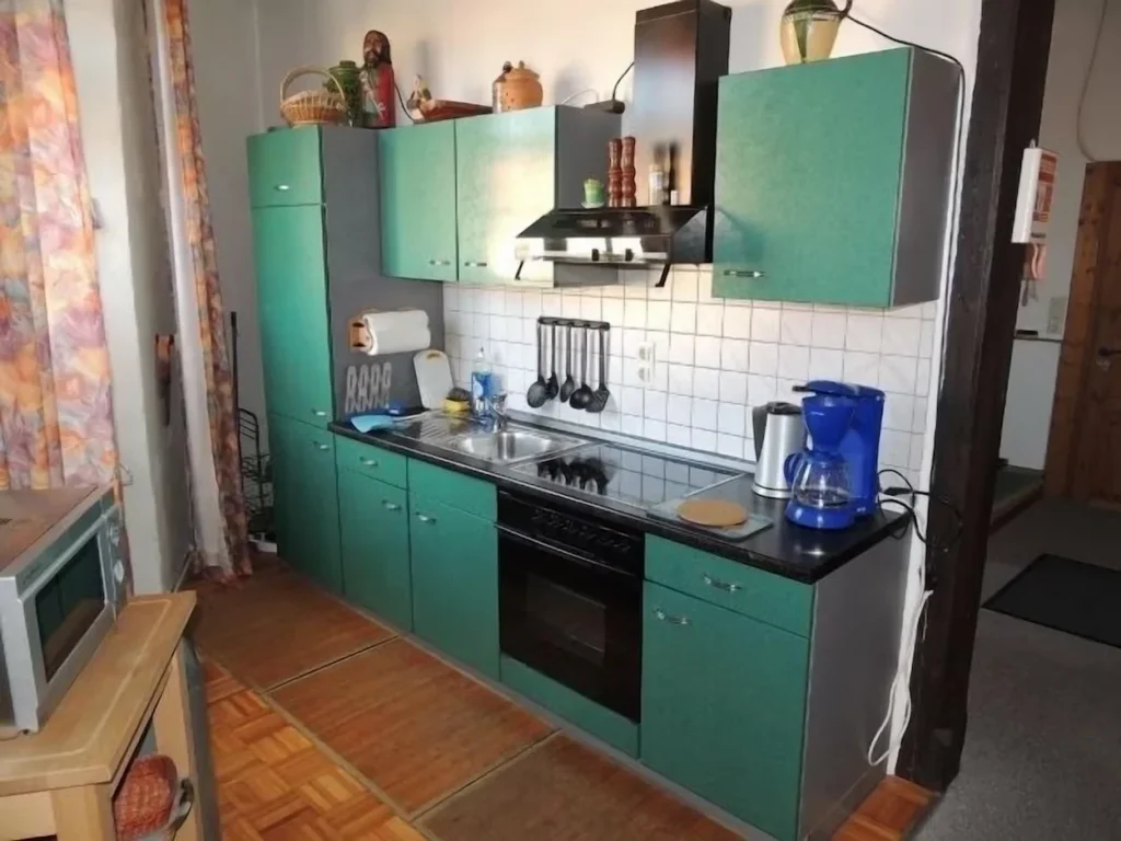 Small kitchen with green cabinets, black countertops, and a white tiled backsplash