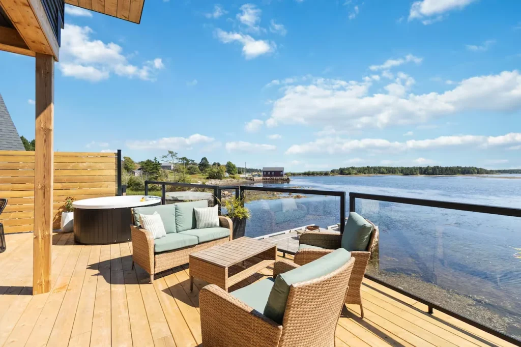 Wooden deck with wicker patio seating and a round hot tub overlooking a river