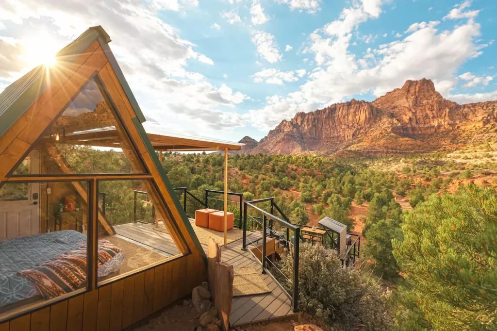 Wooden A-frame cabin with a glass wall balcony facing red canyon mountains