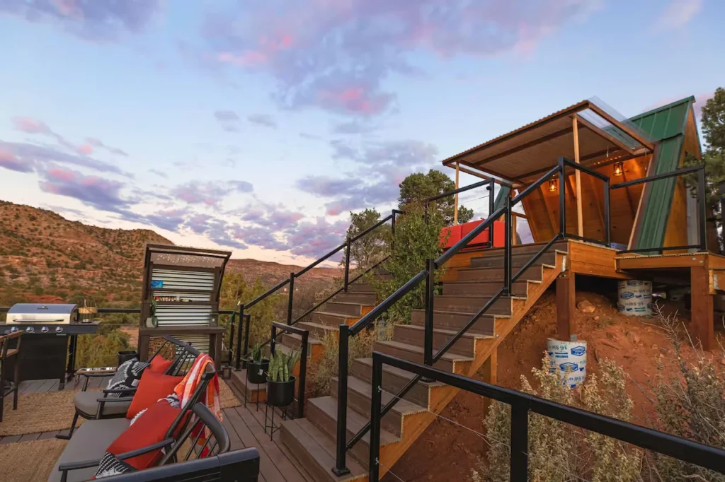 Multi-level wooden deck with outdoor seating leading up to an A-frame cabin at sunset