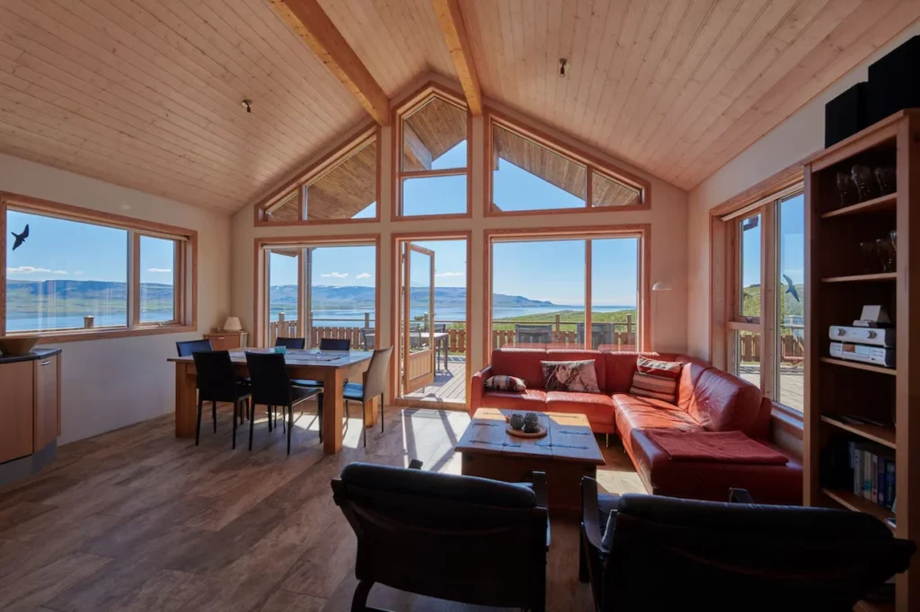 An open-concept cabin living room featuring an orange sectional sofa and a large glass facade facing a lake view