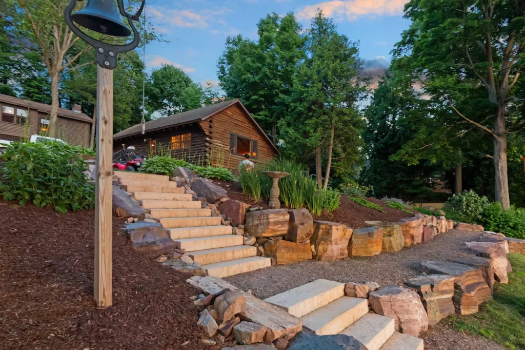 Stone stairs leading up a tiered retaining wall toward a rustic log cabin