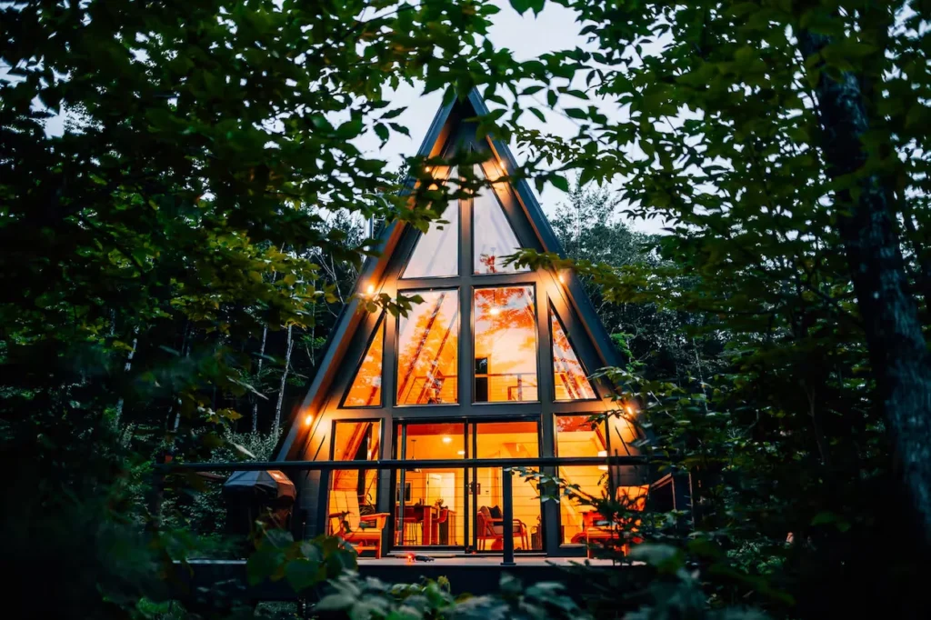 Black metal A-frame cabin with glass doors, a stone fire pit patio, and brilliant orange fall foliage