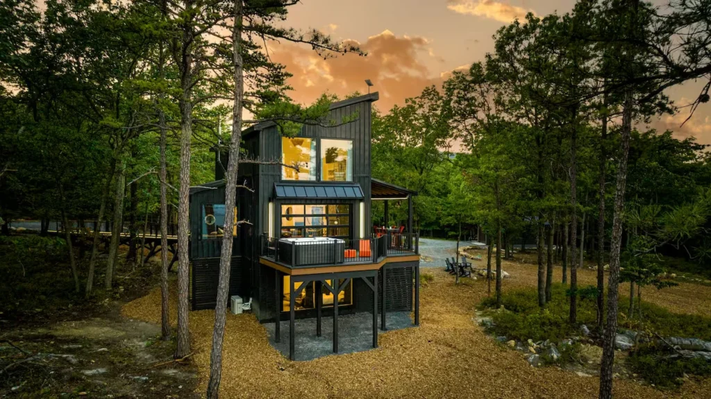 Modern multi-level black cabin with large windows and a balcony hot tub at sunset