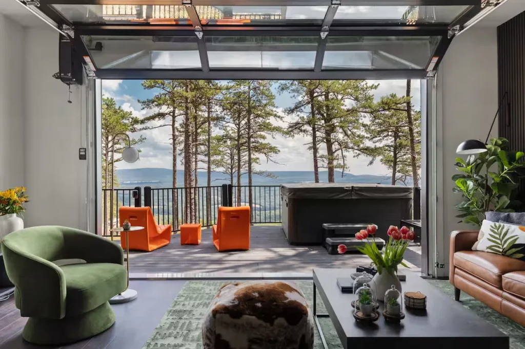 Modern living room open to a deck with hot tub, orange chairs, and a mountain view