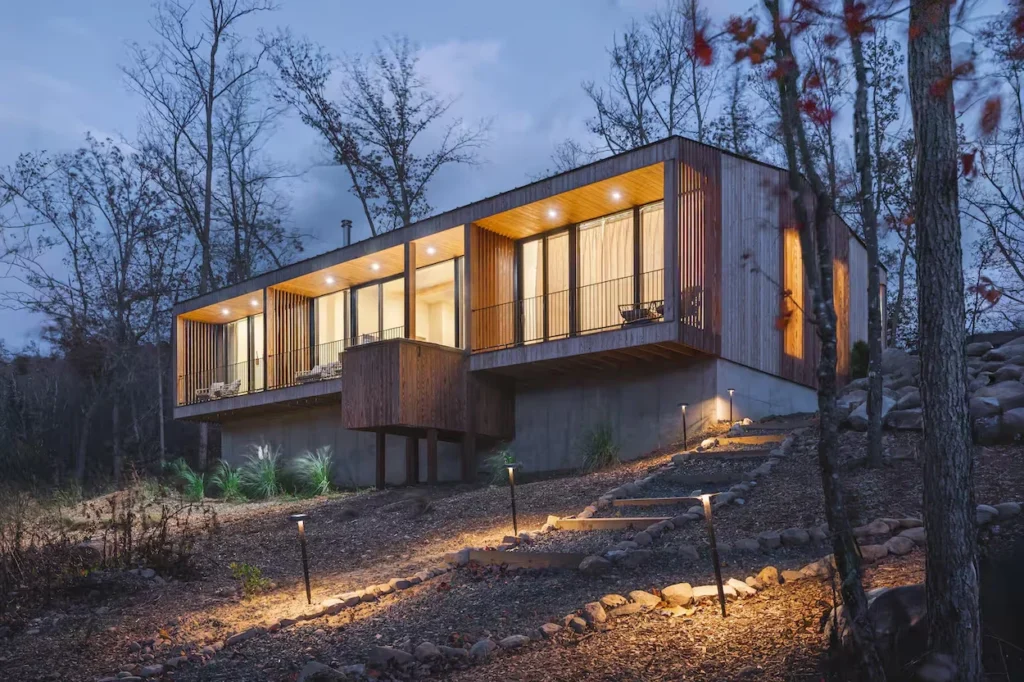 Illuminated modern rectangular wood cabin on a hillside with stone steps at twilight