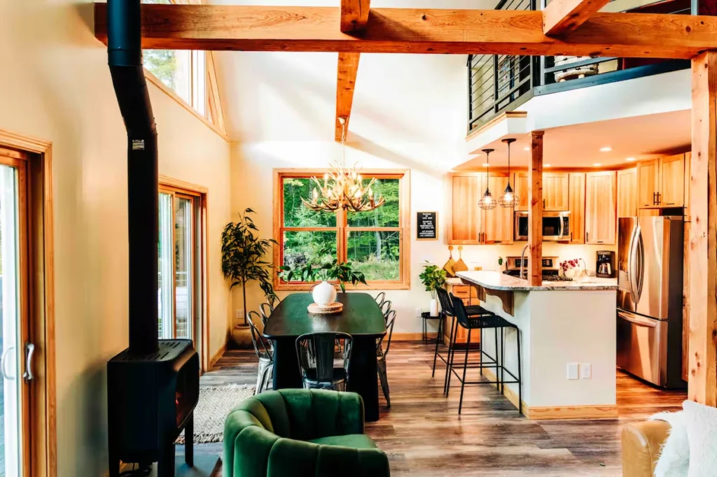 Cabin interior showing an open dining area and kitchen with exposed wooden beams and a wood stove
