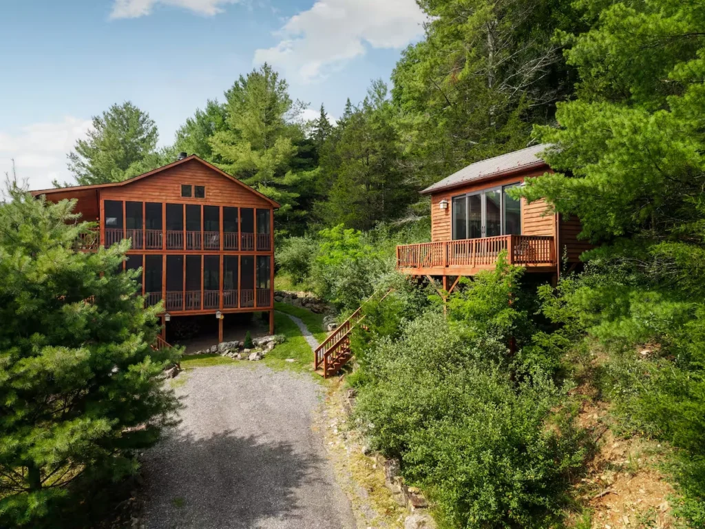 Two wooden cabins with multi-level decks surrounded by dense green pine trees