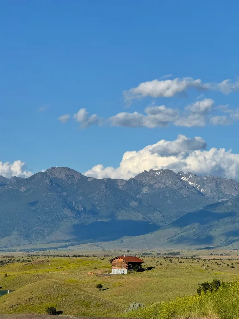 Lone wooden cabin in a vast grassy valley with rugged mountains behind it