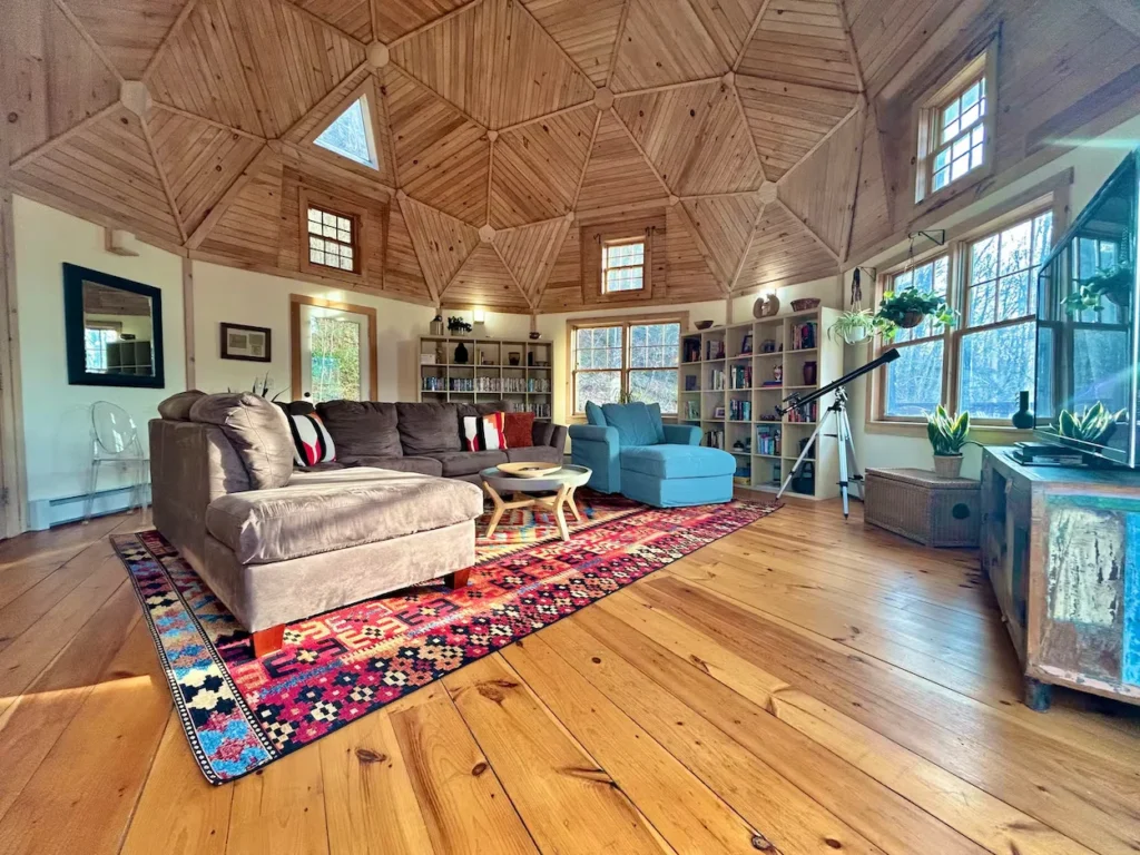 Geodesic dome house living room with geometric pine ceilings, a large rug, and comfortable sofas