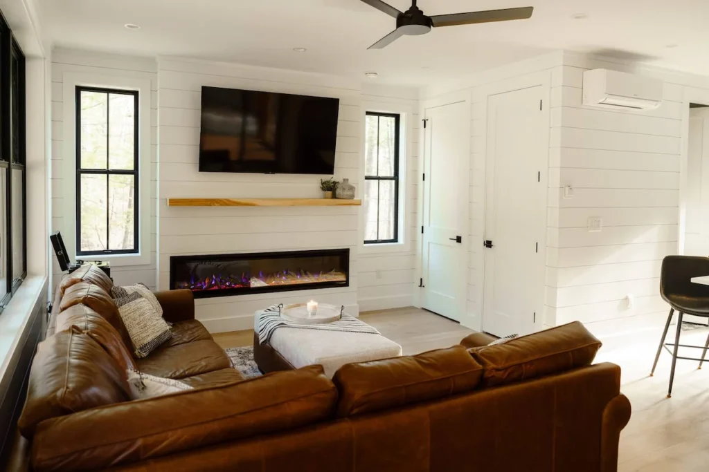 Bright farmhouse living room with shiplap walls, a brown leather sectional, and a linear electric fireplace