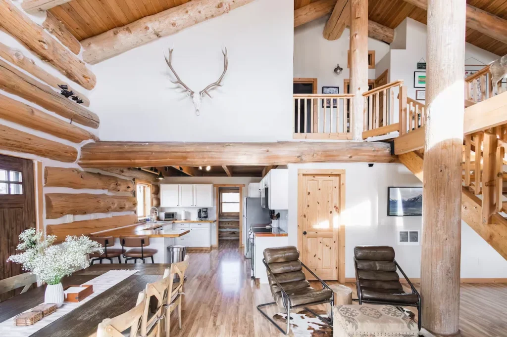 Bright cabin interior with log walls, vaulted ceilings, and a kitchen