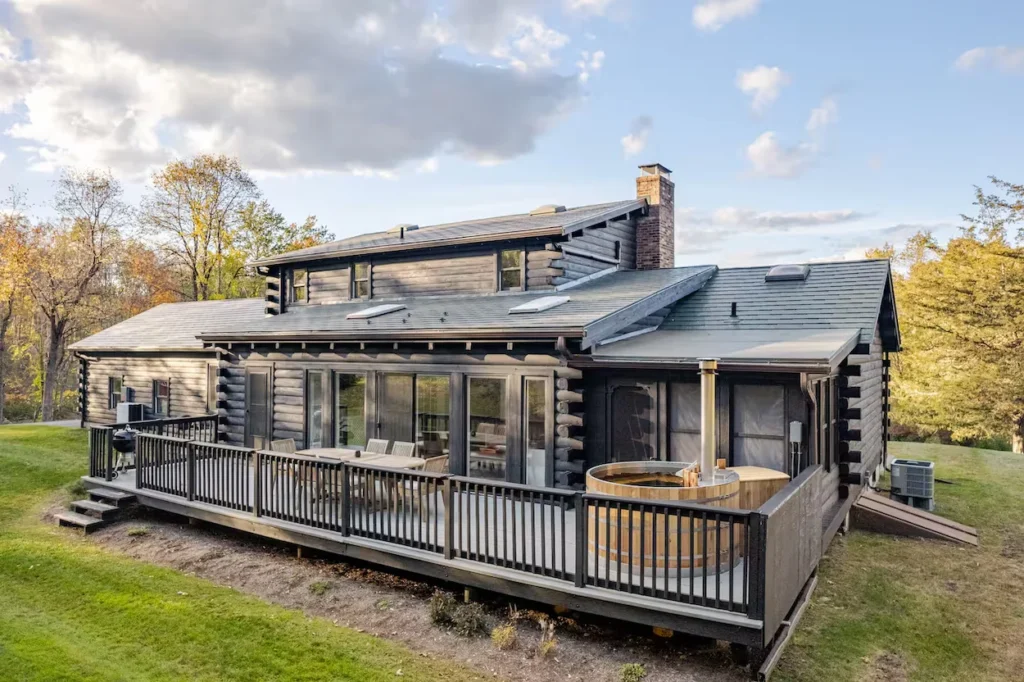Dark stained log cabin in New Milford, Connecticut, with a spacious deck, outdoor dining table, and cedar hot tub