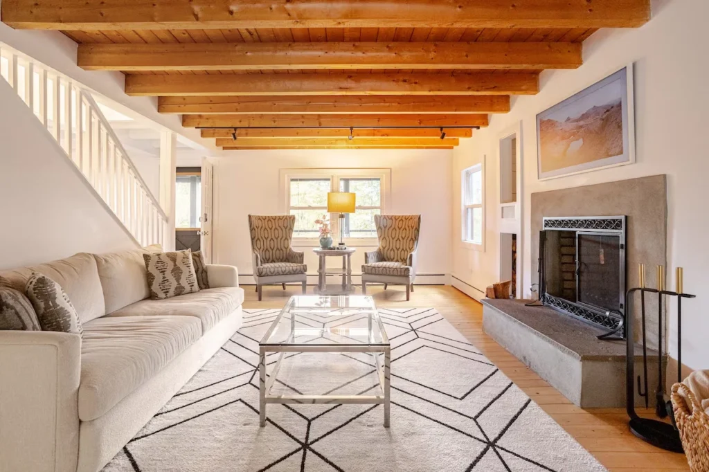 Cabin living room in New Milford, Connecticut, featuring a fireplace, cream sofa, geometric rug, and a wooden ceiling