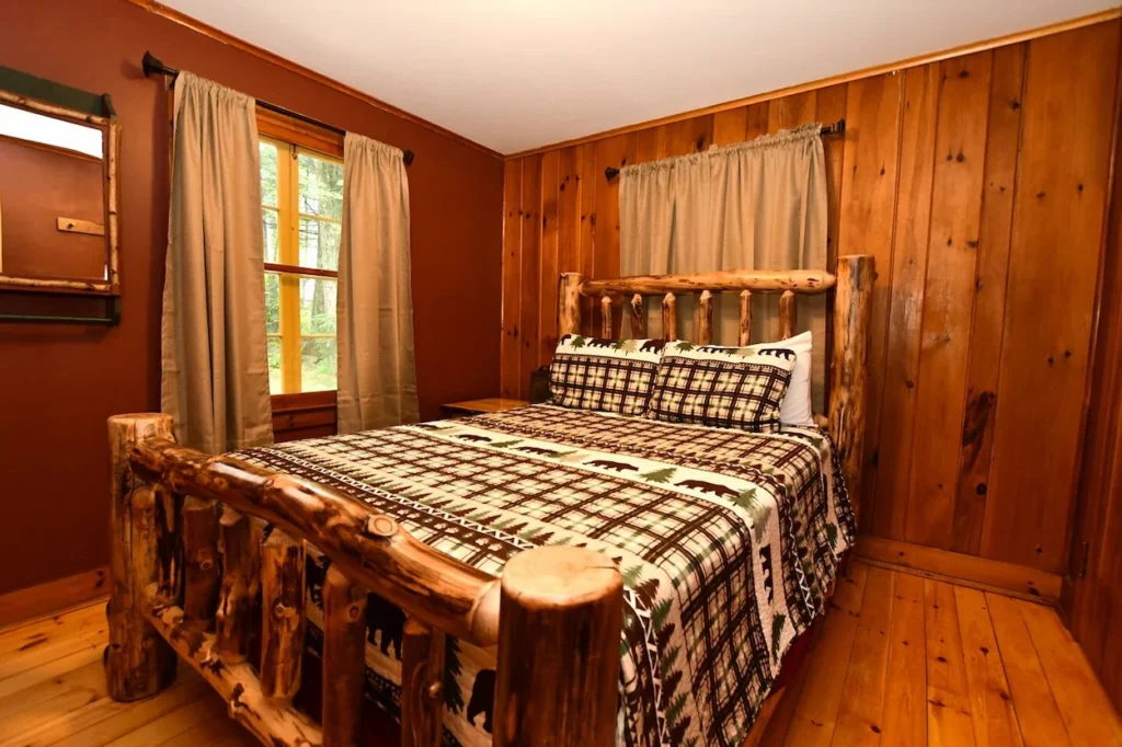 Cabin bedroom featuring a log bed frame, plaid bedding, and knotty pine walls