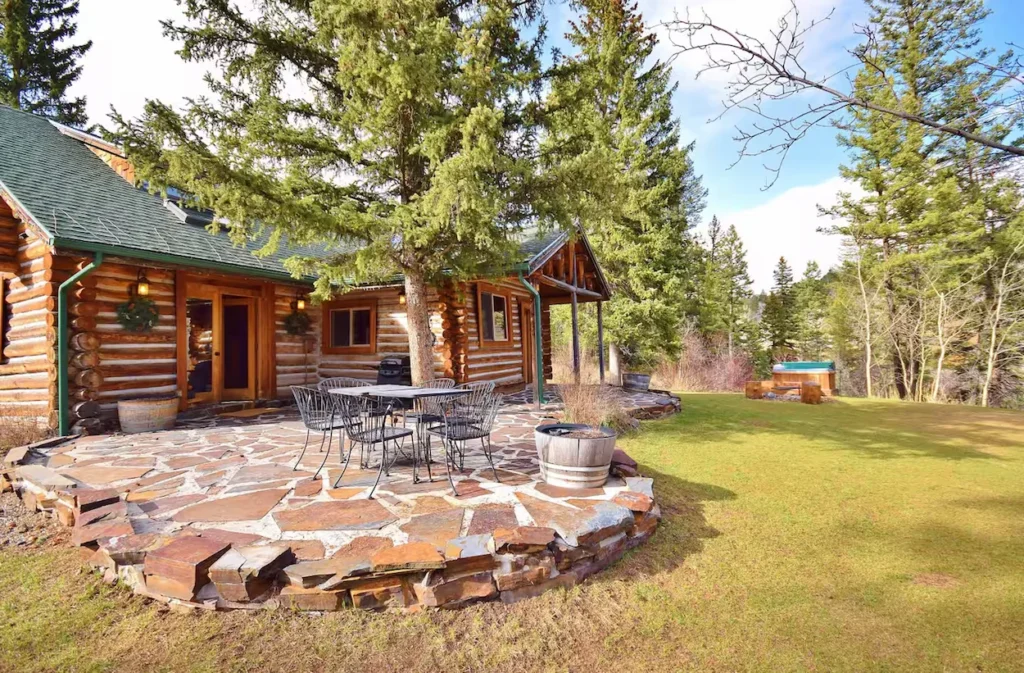 Log cabin backyard with a flagstone patio, outdoor dining set, and grassy lawn