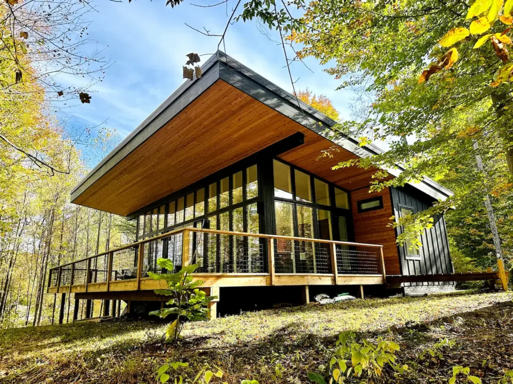 Modern cabin with an angled wood roof, glass walls, and a wrap-around deck