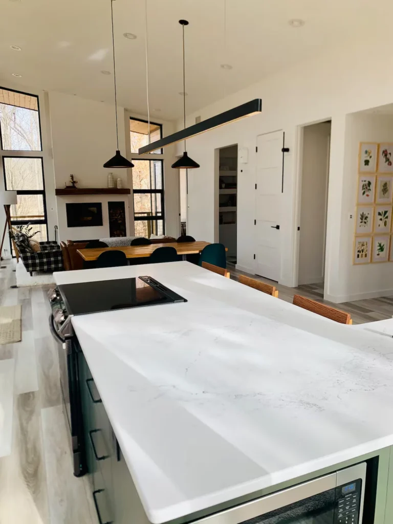 Modern kitchen island with white quartz countertop looking toward a dining table and living room