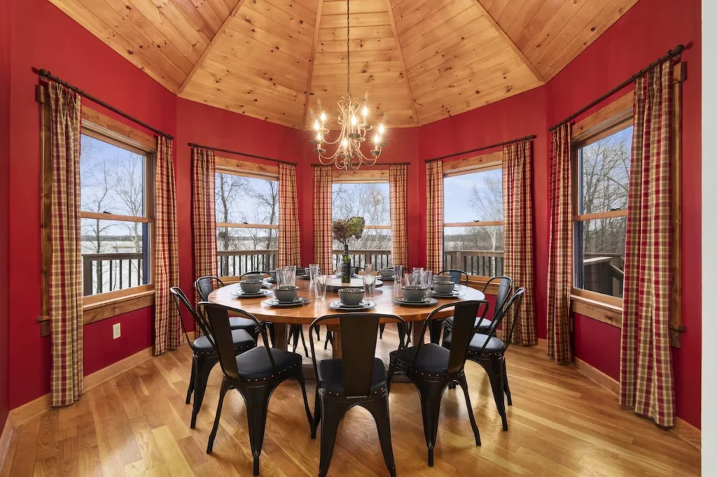 Large round wooden dining table surrounded by black metal chairs in an octagonal red-walled dining room