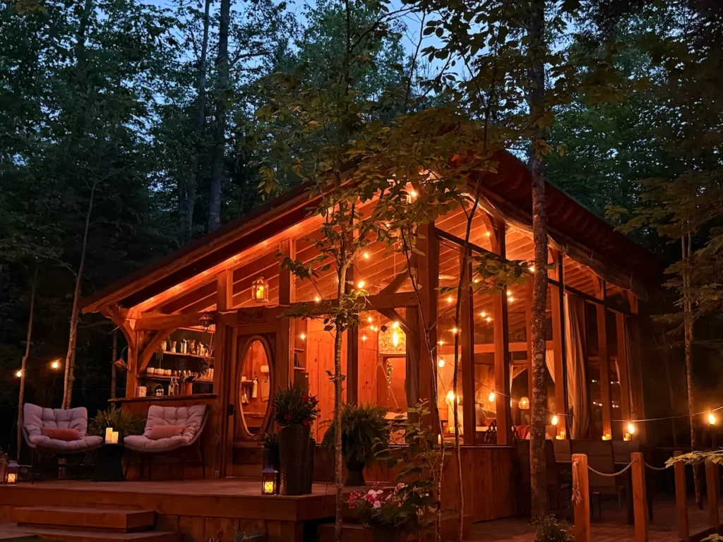 Illuminated glass-walled cabin with string lights surrounded by woods
