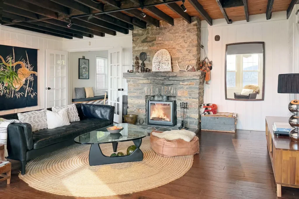 Cozy cabin living room featuring a stone fireplace, black leather sofa, and exposed ceiling beams