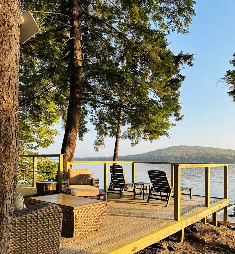 Wooden lakefront deck with wicker lounge furniture and views of water and forested hills