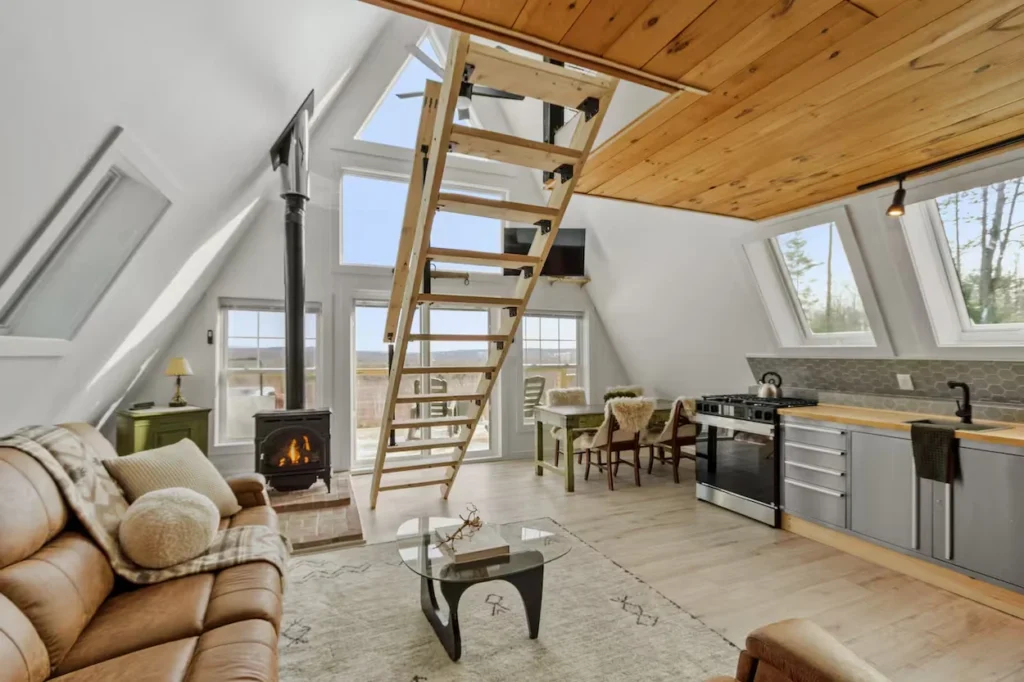 A-frame cabin interior with a leather sofa, wood stove, central stairs, and kitchen