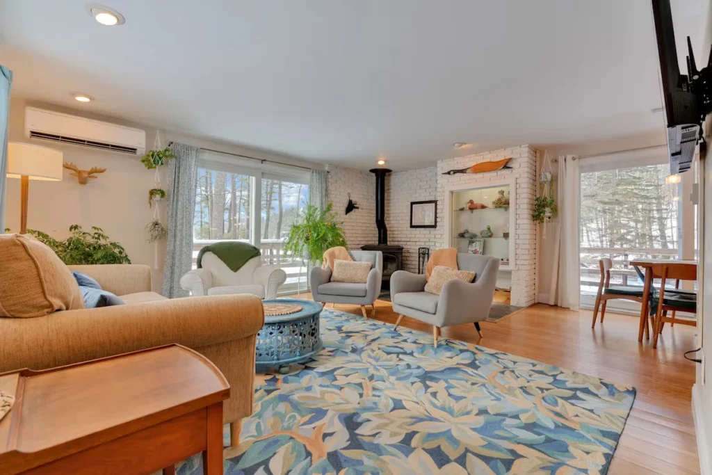 Bright cabin living room with a blue floral rug, gray armchairs, and a wood stove